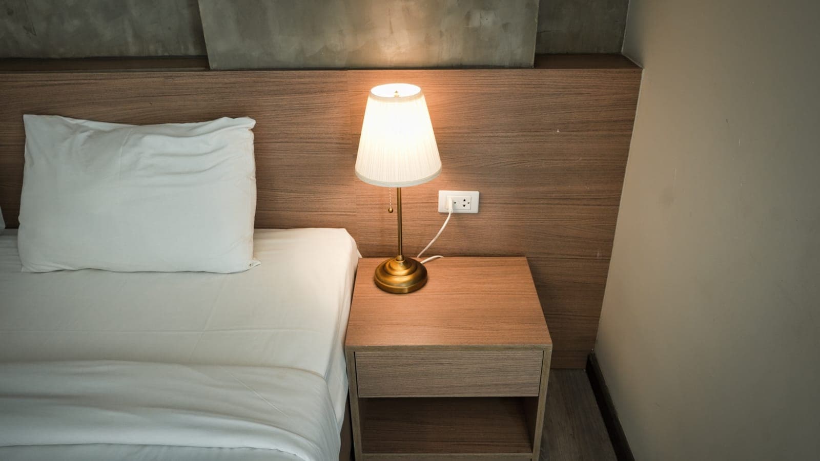 A lamp on a wooden nightstand beside a bed in a quiet bedroom